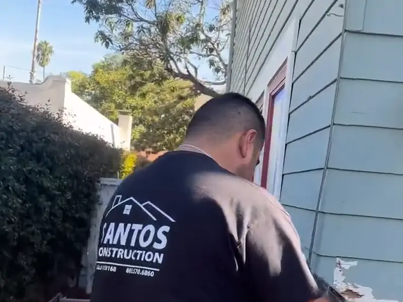 Santos worker repairing siding on a house